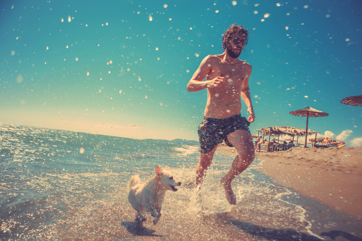 Joven corriendo junto a su perro en la playa (© Istockphoto)